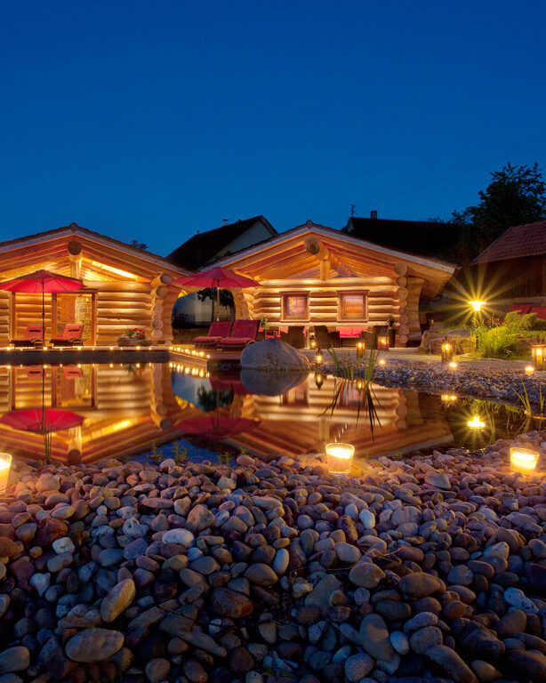 Zwei elegant beleuchtete Blockhütten an dem nächtlichen Natur-Schwimmteich in der Naturspa des Hotels Konradshof.