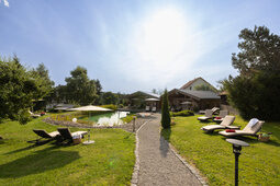 Ein weitläufiger grüner Garten mit Liegestühlen und Sonnenschirmen vor dem Naturschwimmteich im Hotel Konradshof in Besenfeld