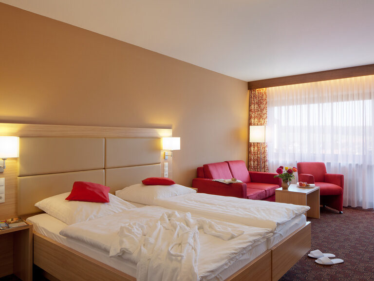 Ein geräumiges Schlafzimmer im Hotel Konradshof mit einem großen Bett und einer gemütlicher Couch und Sessel.