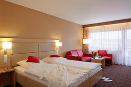 Ein geräumiges Schlafzimmer im Hotel Konradshof mit einem großen Bett und einer gemütlicher Couch und Sessel.