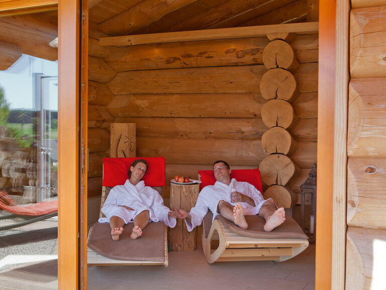 Händchen haltendes Wellness-Paar entspannt auf einer Holzliege und im Hotel Konradshof im Nordschwarzwald